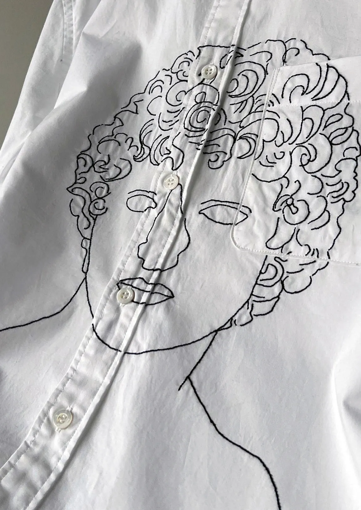 Embroidered line drawing of a face on a white shirt