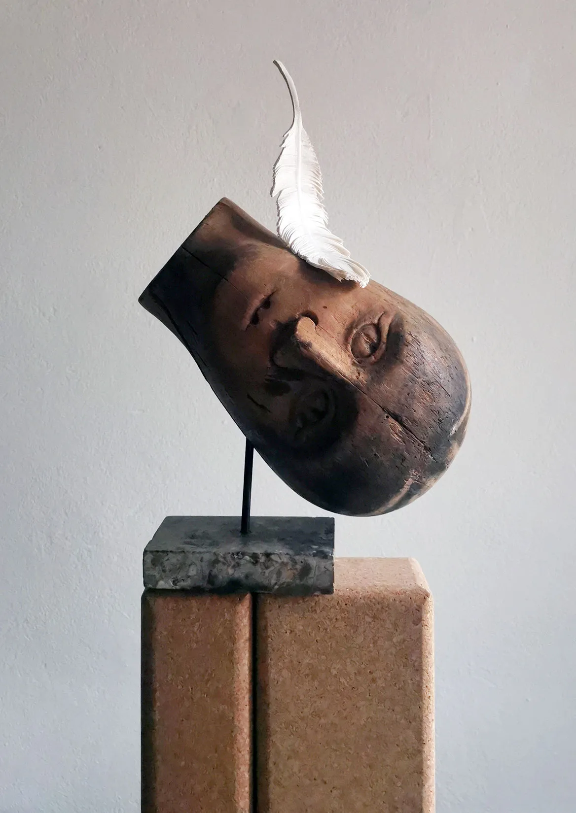Sculptural head with a leather feather on a stone plinth